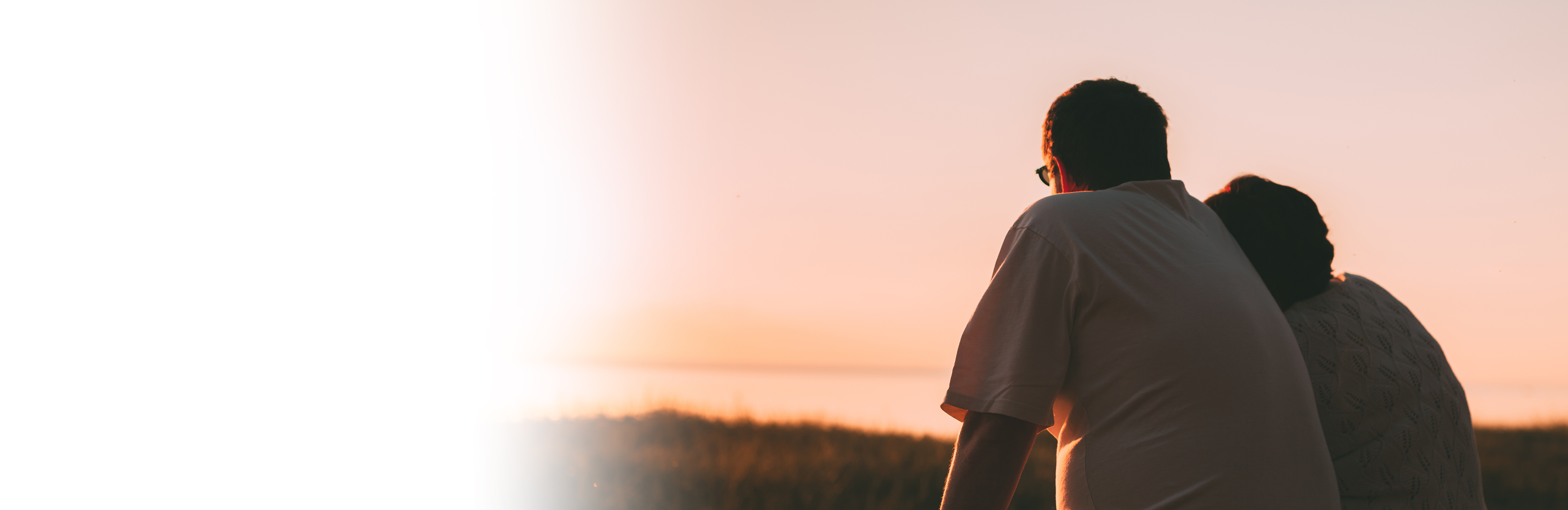 Two older adults sitting and watching sunset, from behind