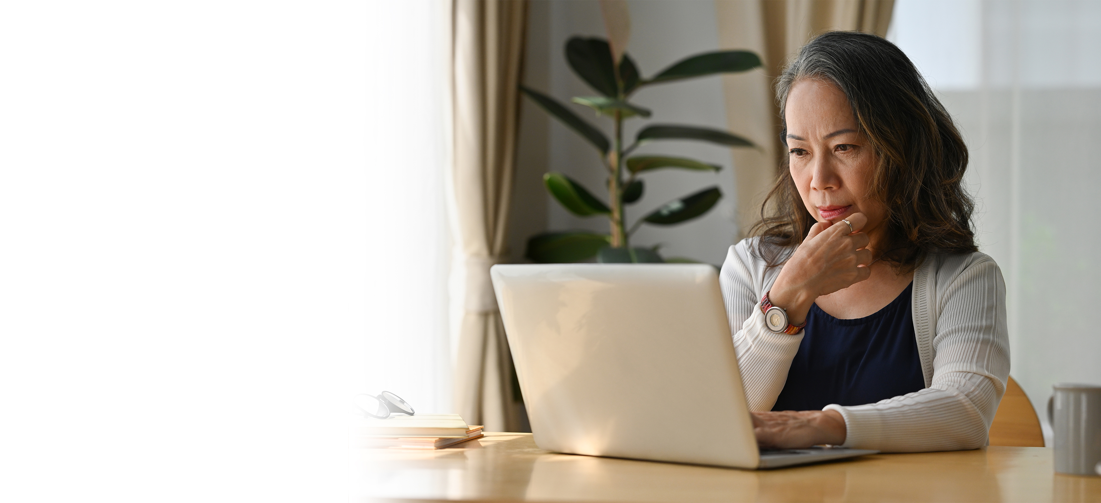 Older Asian lady looking at laptop with contemplative pose